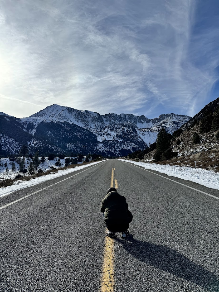 Ben crouching on the center line of a mountain road, with snowy peaks beyond.